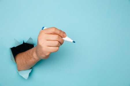 A man writes a marker on a broken blue paper wall.の写真素材