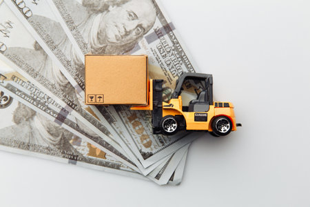 Mini model of forklift with carton box and dollar bills isolated on white background. Logistics and delivery concept. Top viewの写真素材