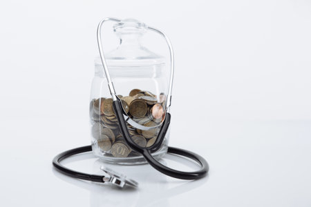 Coins money in glass bottle with stethoscope on white table. Save money for Medical insurance and Health care conceptの写真素材