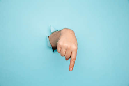 Finger pointing down through torn blue paper wall. Hand gestures of direction