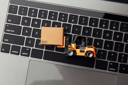 Mini model of forklift with box on laptop. Logistics and delivery concept