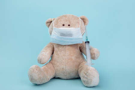 Stuffed Bear animal in mask with syringe isolated on blue. Children healthcare conceptの写真素材