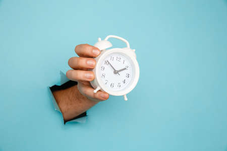 Hand holds alarm clock through a paper hole. Time management and deadline conceptの写真素材