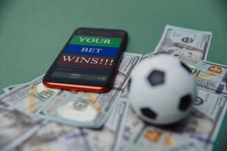 Football Business Concept. Ball and smartphone with bet application on dollar bills and green background. Soccer gambling money conceptの写真素材