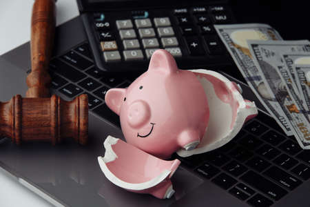 Broken piggy bank, money and wooden gavel on keyboard close-up. Auction and bankruptcy concept