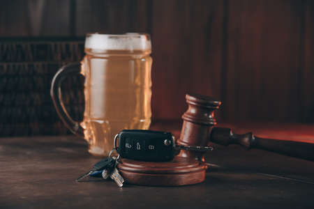 Glass of beer, car keys and judge gavel on a wooden table. Alcohol and driving abilityの写真素材