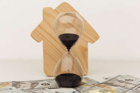 Wooden house and clock on dollar banknotes close-up. Buying or selling real estate