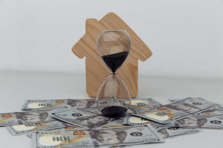 Wooden house and clock on dollar banknotes. Buying or selling real estateの写真素材