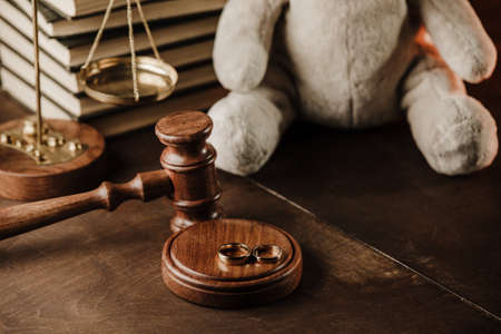 Divorce concept. Wooden gavel, rings and teddy bear as symbol of child on a deskの写真素材