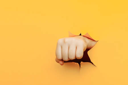Fist punching through yellow paper background. Threat, fight and combat sportsの写真素材