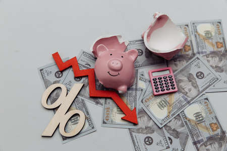 Bankruptcy concept. Broken piggy bank on dollar banknotes and arrow down on dollar banknotes