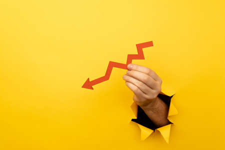 Hand with a red arrow down through a yellow paper holeの写真素材