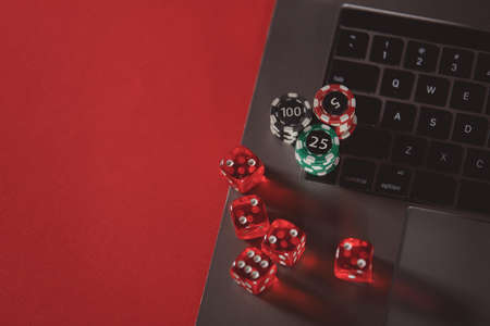 Stacks of poker chips, dices and laptop on a red background. Poker online concept