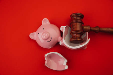 Broken pink piggy bank with wooden judge gavel on a red background. Law and bankruptcy conceptの写真素材