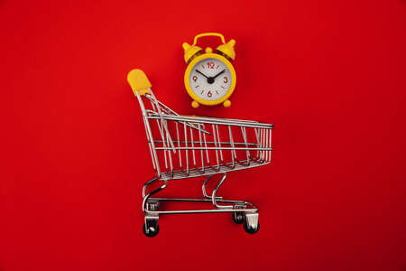 Shopping cart and yellow alarm clock isolated on redの写真素材