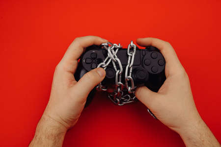 Game addiction concept. Hands of a young man holds a game controller is tied by chain
