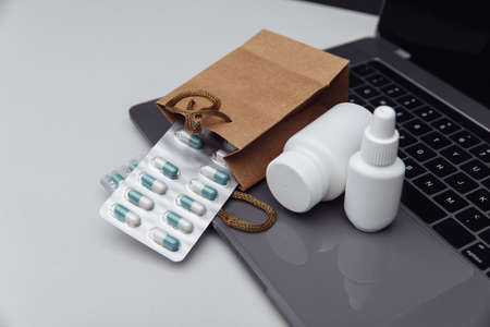 Online pharmacy concept. Pills and spray containers and buff paper bags on the laptopの写真素材