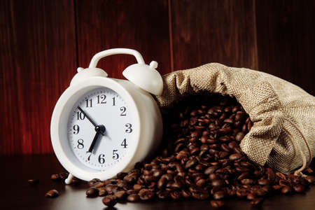 A white alarm clock and coffee beans in a bag on wooden table close-upの写真素材
