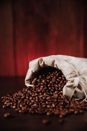 Coffee beans scattered of the bag on wooden table. Vertical imageの写真素材
