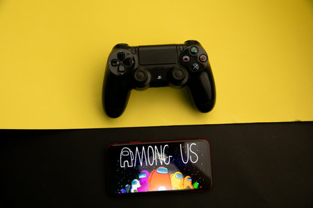Tula, Russia - April 08, 2021: Among Us logo on iPhone display and PS gamepad