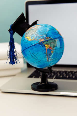 International online education concept. Globe with graduation hat on laptop backgroundの写真素材