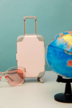 Travel concept. Plastic travel suitcase, pink glasses and globe. Vertical imageの写真素材