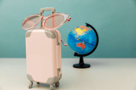Plastic travel luggage, pink glasses and globe on a table. Traveling conceptの写真素材