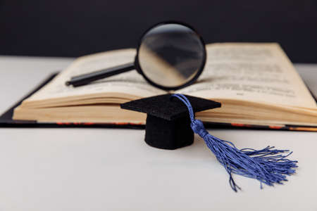 Graduation cap and magnifier on open book on white table. Education conceptの写真素材