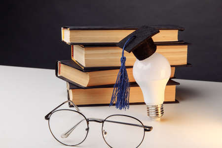 Graduation cap on lightbulb with books on a white table. Education and science conceptの写真素材