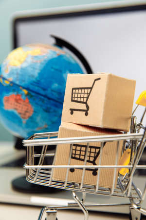 Online shopping and ecommerce concept. Globe and supermarket shopping cart with boxes on a laptop...