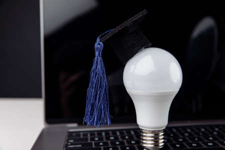 Online education concept. Graduation cap on light bulb in front of laptop screenの写真素材