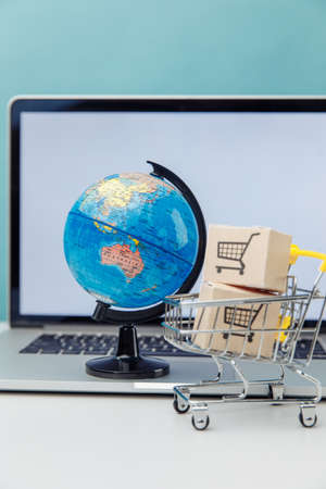 Online shopping and ecommerce concept. Globe and supermarket shopping cart with boxes near laptop. Vertical imageの写真素材