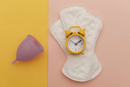 Menstrual pad, pads and alarm clock on colorful background. Top view. Menstruation cycle period conceptの写真素材