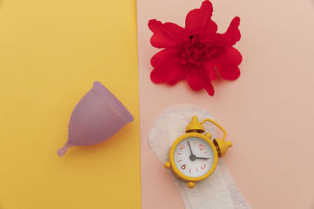 Menstrual cup with red flower and pads with alarm clock. Top view. Modern way of womens hygiene conceptの写真素材