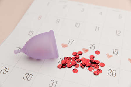 Calendar and menstrual cup with red shining sequins. Concept of critical days and hygieneの写真素材