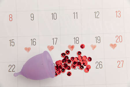 Calendar and menstrual cup with red shining sequins. Concept of critical days and womens hygieneの写真素材
