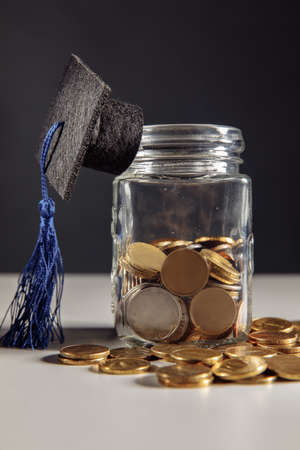 Graduation hat on jar with coins. Scholarship money concept. Vertical imageの写真素材