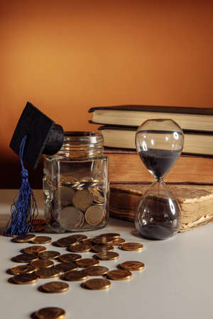Jar with coins, graduation hat and hourglass. Savings and education themeの写真素材
