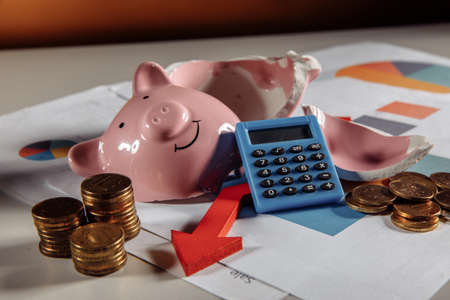 A broken piggy with stuck of coins, calculator and arrow down on business diagram. Business conceptの写真素材