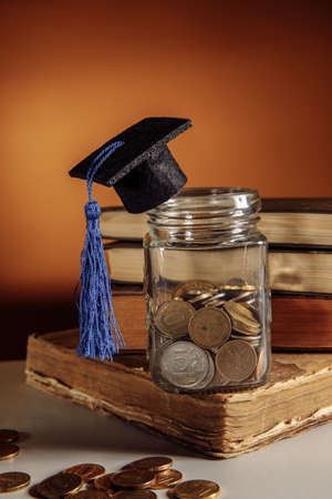Glass jar with coins and graduation hat on books, scholarship concept. Vertical image
