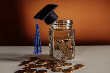 Jar with money and graduation hat on a table, scholarship and savings conceptの写真素材