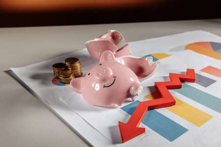 A broken piggy bank with coins and a red arrow down lie on diagram