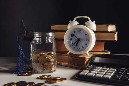 Savings for education concept. Glass jar with money and graduation hat near white alarm clockの写真素材