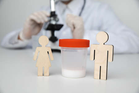 A plastic jar with sperm for semen analysis with a wooden couple. Planning pregnancy and health...