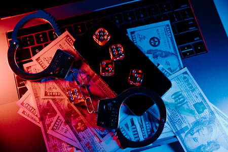 Handcuffs, smartphone and playing dice on keyboard in neon light. Illegal casino and punishment conceptの写真素材