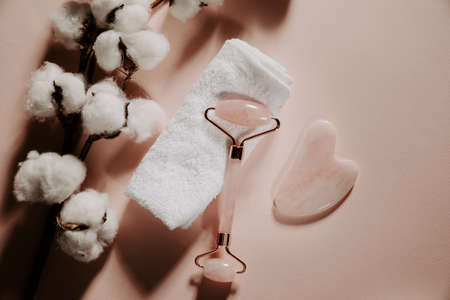 Skin care concept. Jade face roller for beauty facial massage therapy with towel and cotton on a pink background.の写真素材