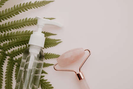 Pink quartz face massage roller, essence in a bottle and fern leaf on pink tableの写真素材