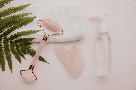 Essence in a bottle and roller, gua sha massage scraper on a pink background. Top view. Selfcare, beauty and health conceptの写真素材