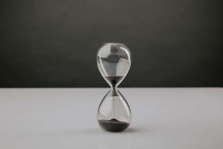 Modern hourglass on a table with dark background, deadline concept