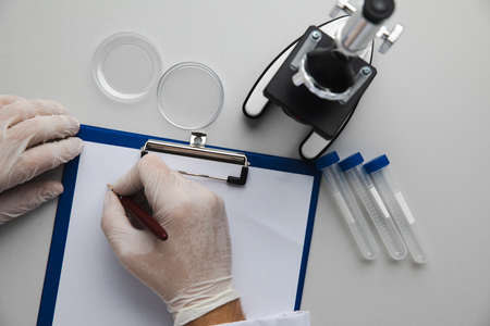 Hands of medical doctor making notes at his office, test-tubes and microscope on a table. Top viewの写真素材